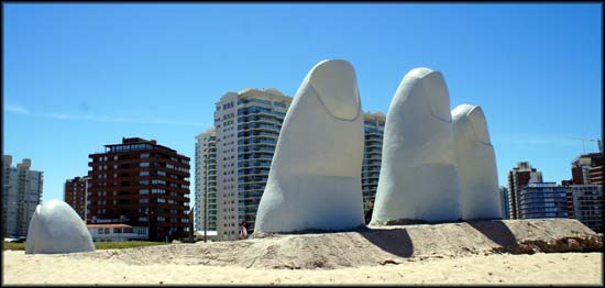 Escultura na areia da praia, prédios ao fundo